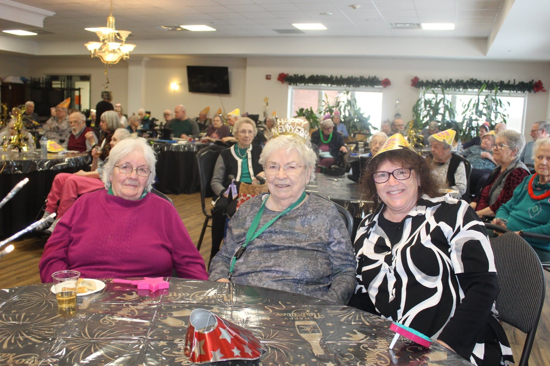 Three women smiling at a banquet table in a decorated community hall