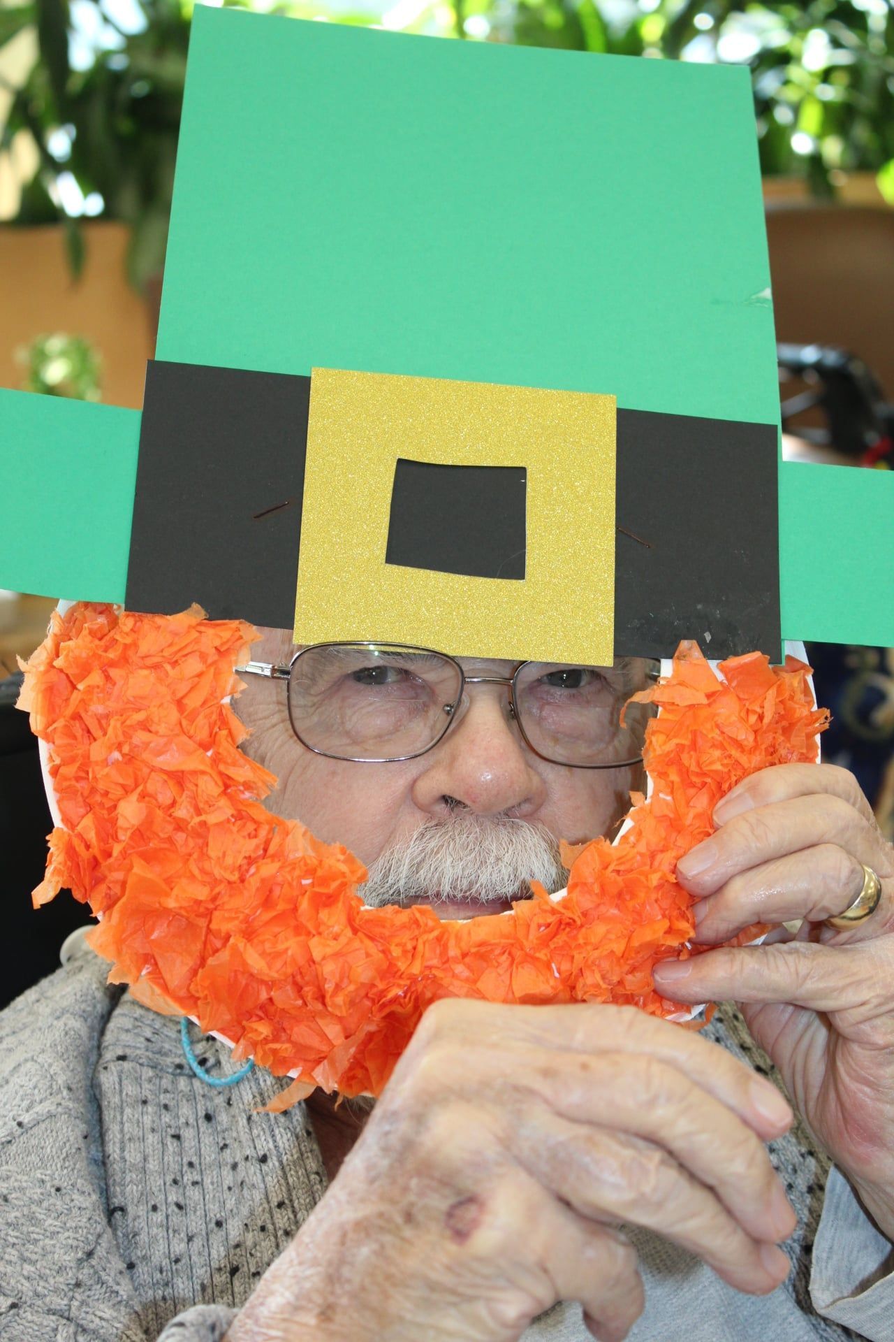 Person wearing a leprechaun hat and orange beard, adjusting glasses indoors