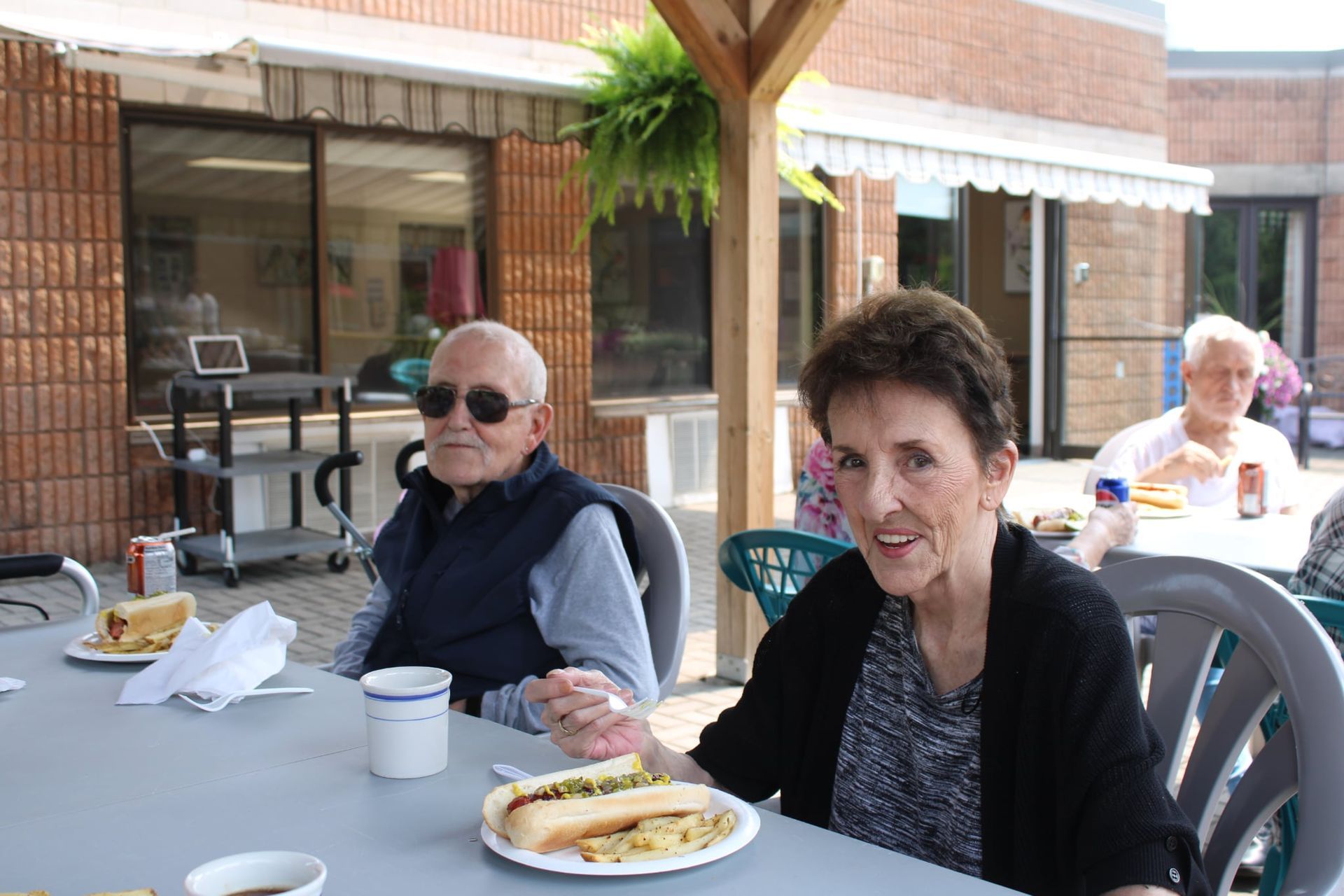 Two people sit at an outdoor table with food and drinks on a patio.