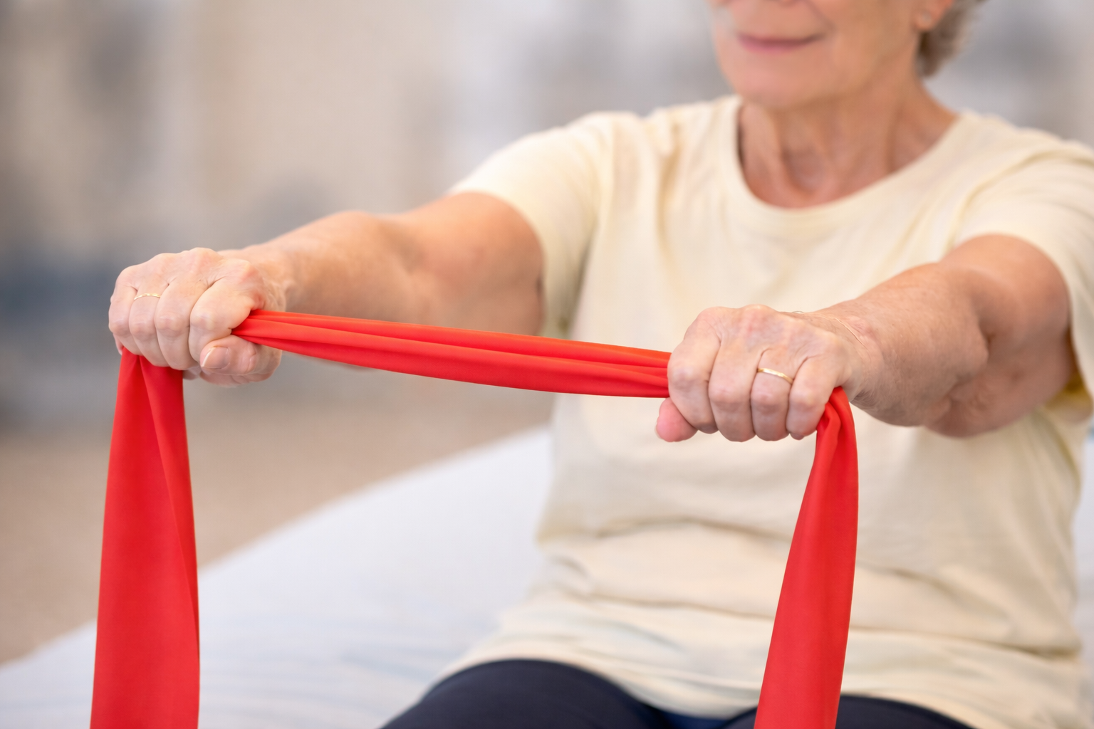 Person stretching a red resistance band while seated indoors