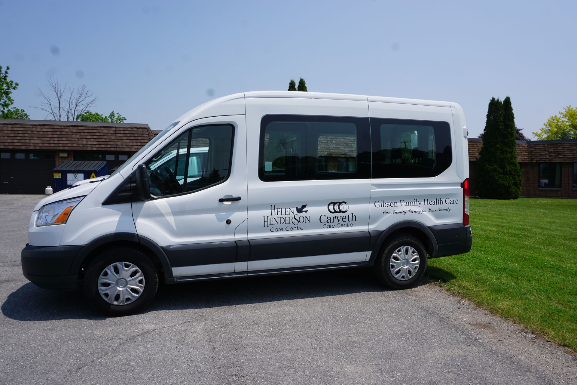 White shuttle van parked on a gravel drive beside a grassy lawn and building
