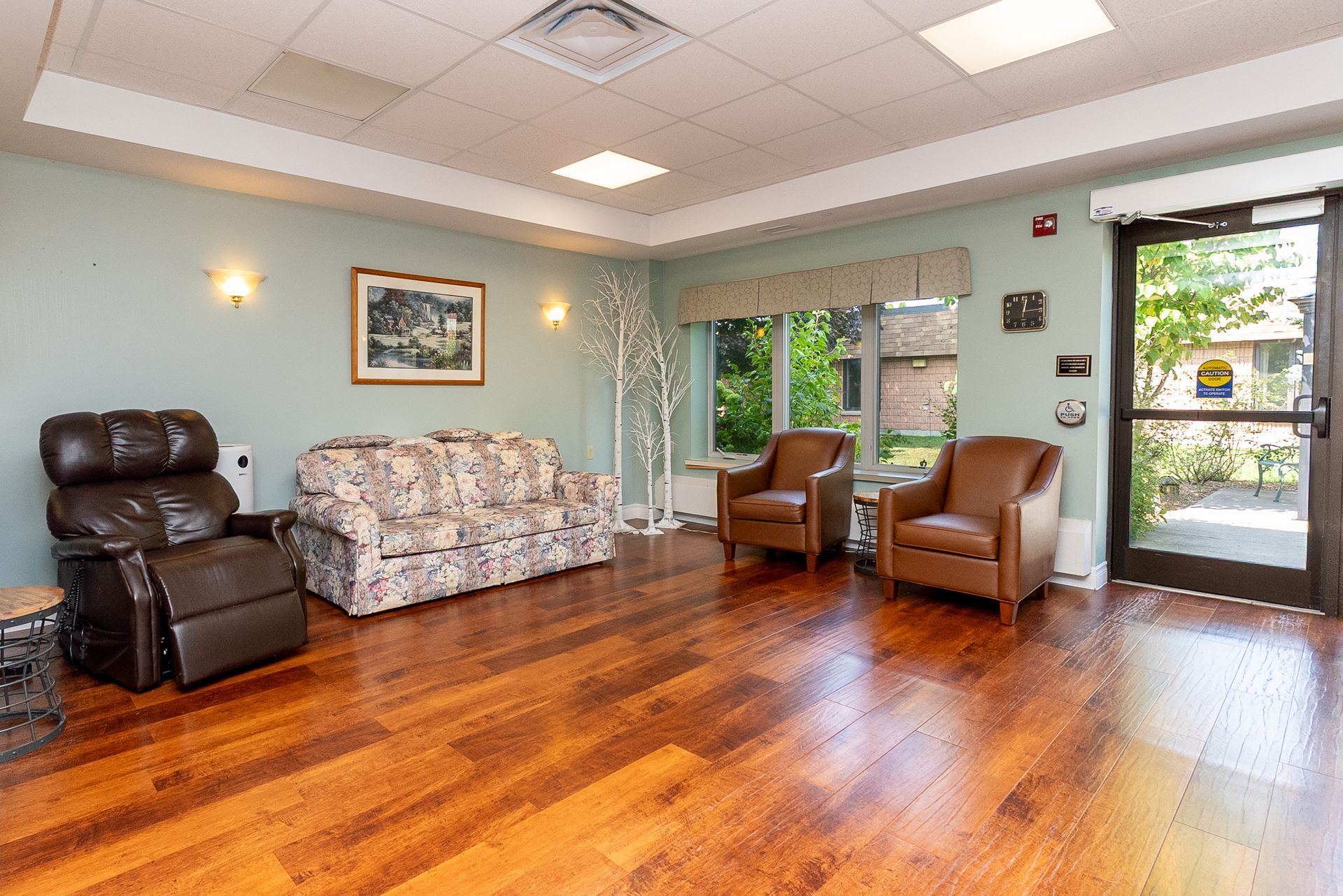 Spacious waiting room with wood floors, floral couch, leather chairs, and large windows.