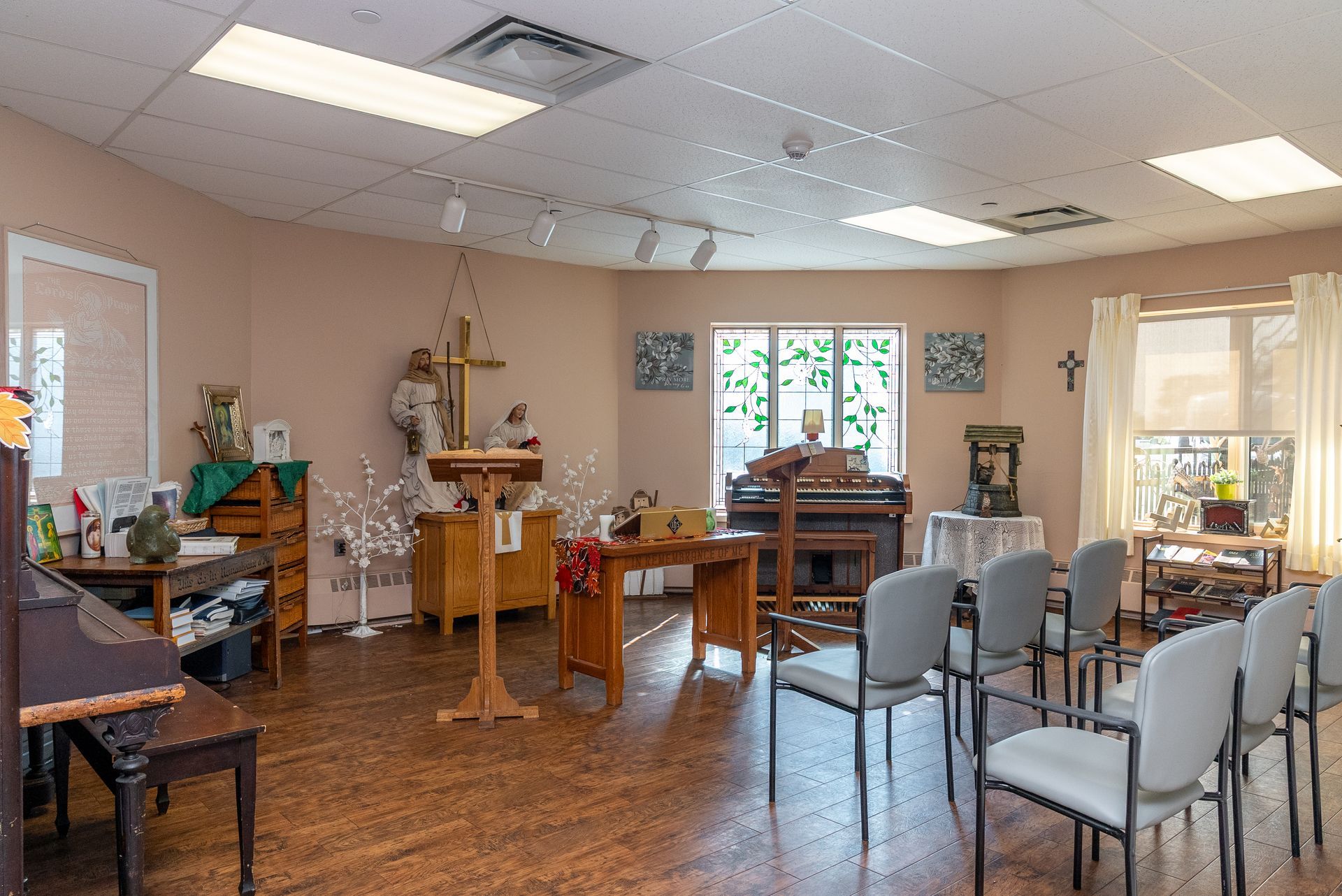 Small chapel or prayer room with altar, wooden furnishings, and rows of chairs under bright ceiling lights.