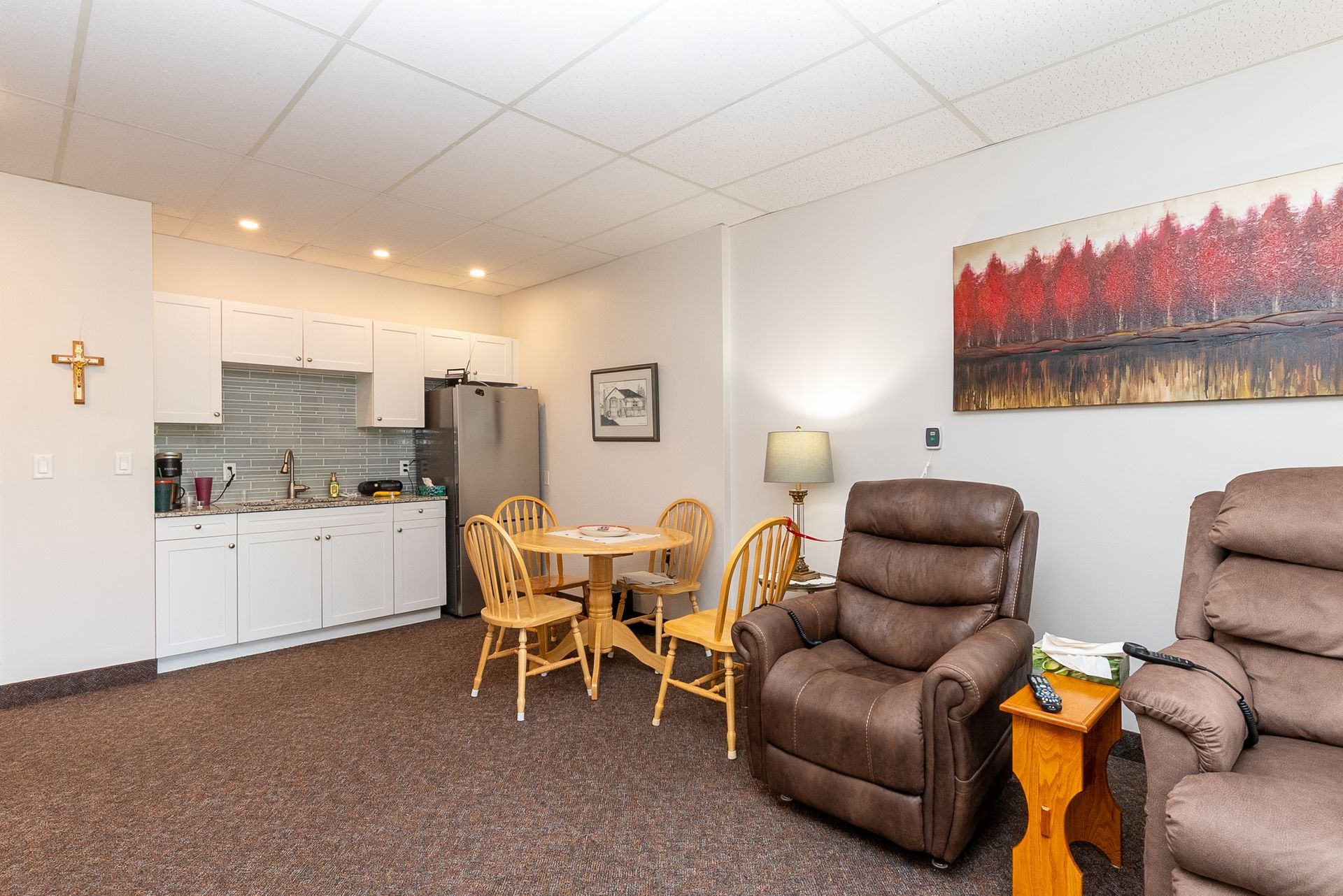 Small living room with kitchenette, brown recliners, round table, and wall art.