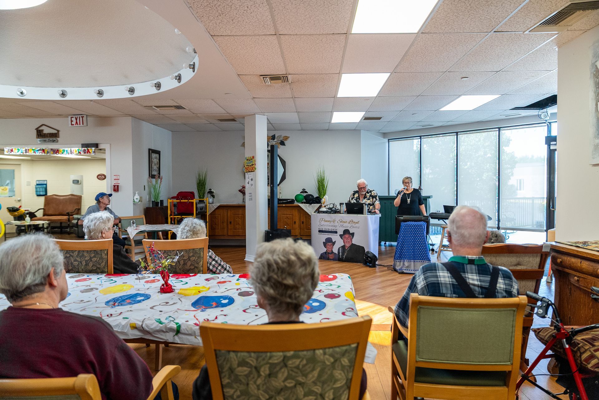 Residents seated in a common room watching a small musical performance near large windows
