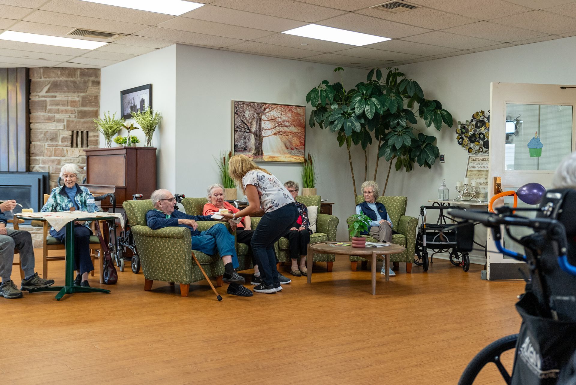 People seated and chatting in a cozy common room with chairs, plants, and warm lighting