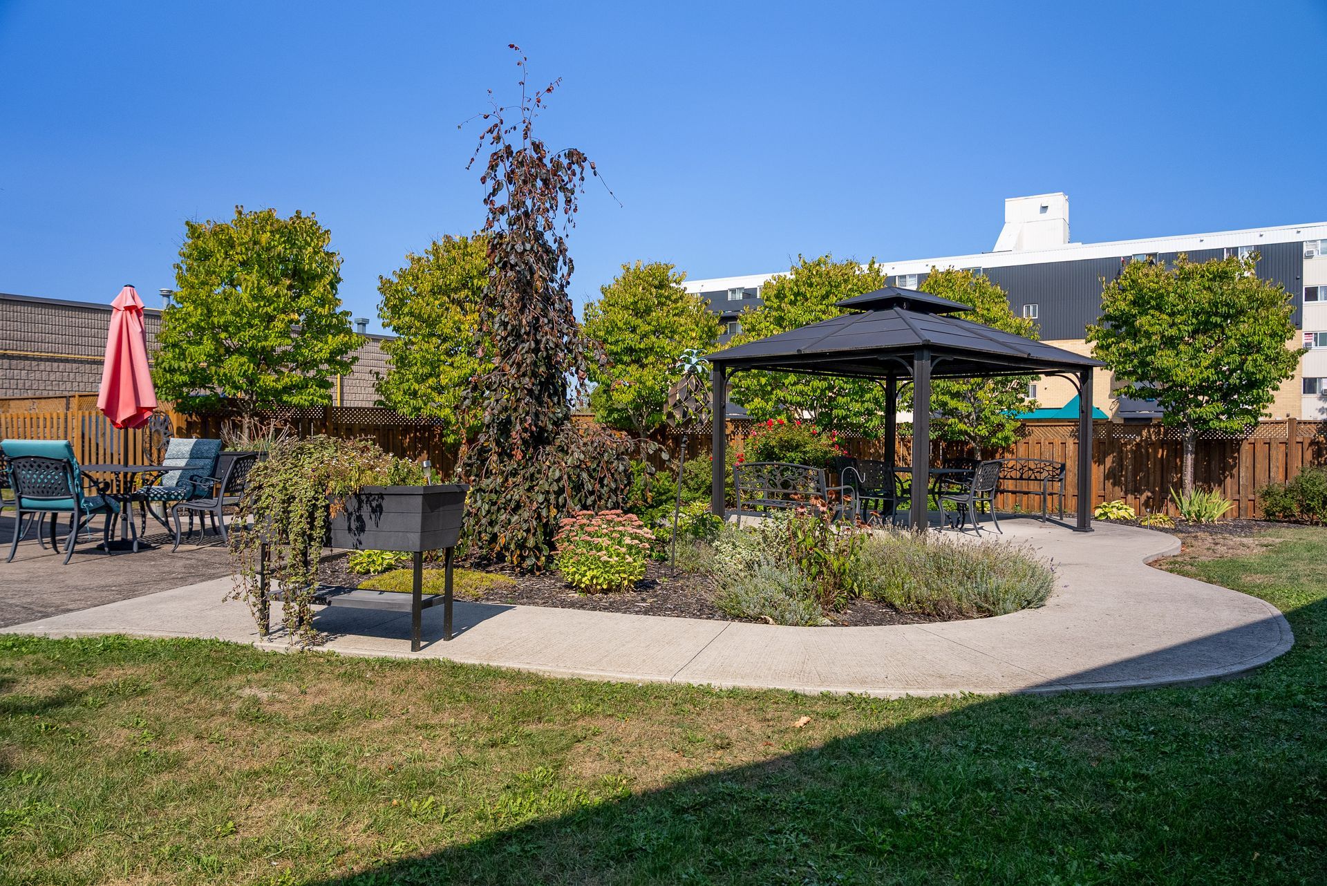 Backyard patio with gazebo, tables, chairs, and a winding gravel path among shrubs and trees