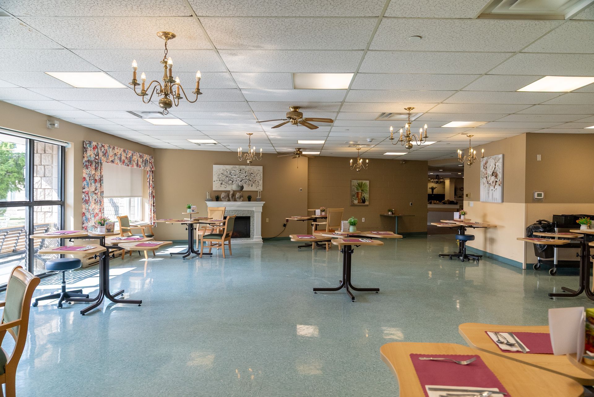 Empty cafeteria with round tables, blue carpet, and large windows along the left wall.