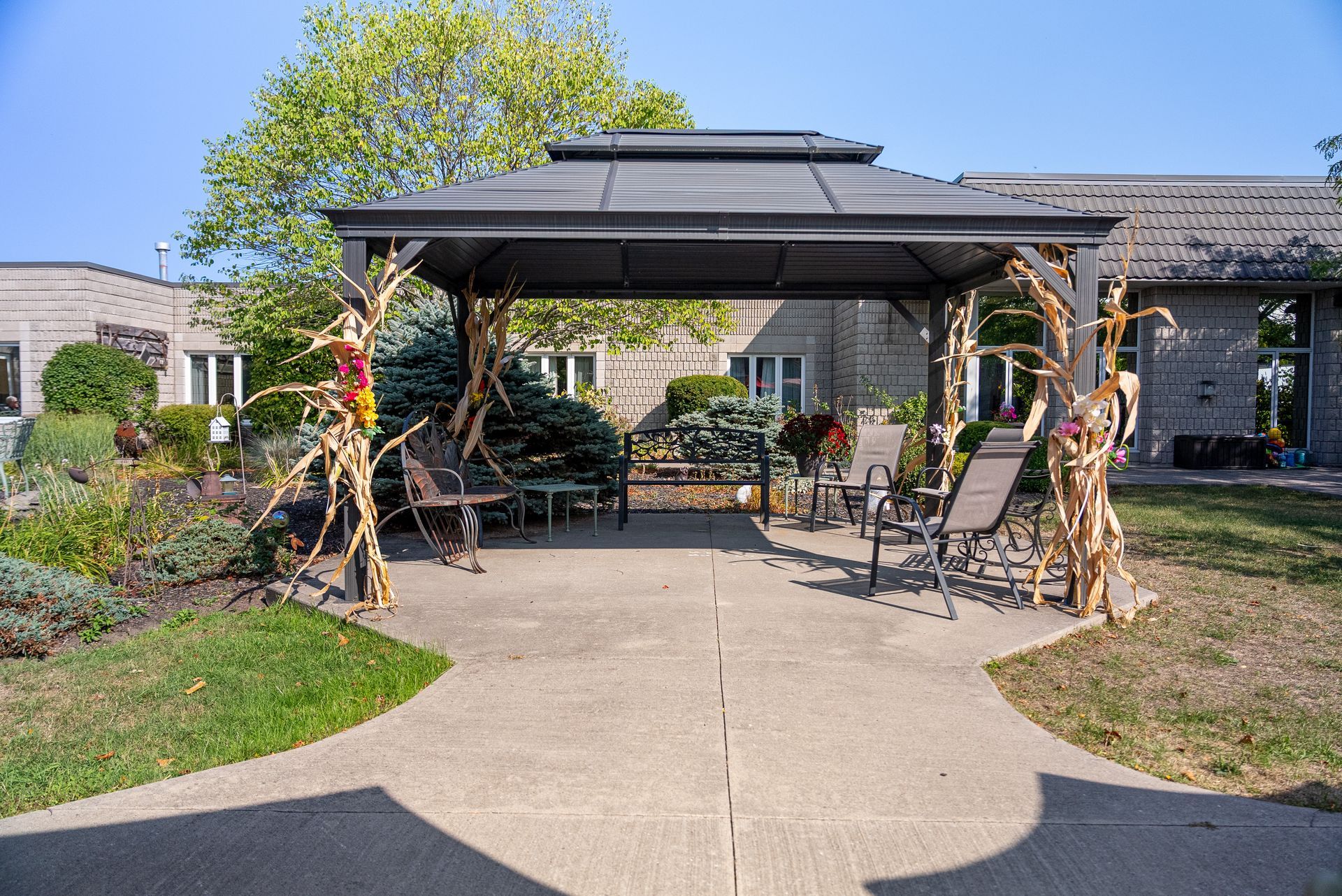 Outdoor courtyard with a shaded gazebo, patio tables and chairs, and landscaped paths under a blue sky