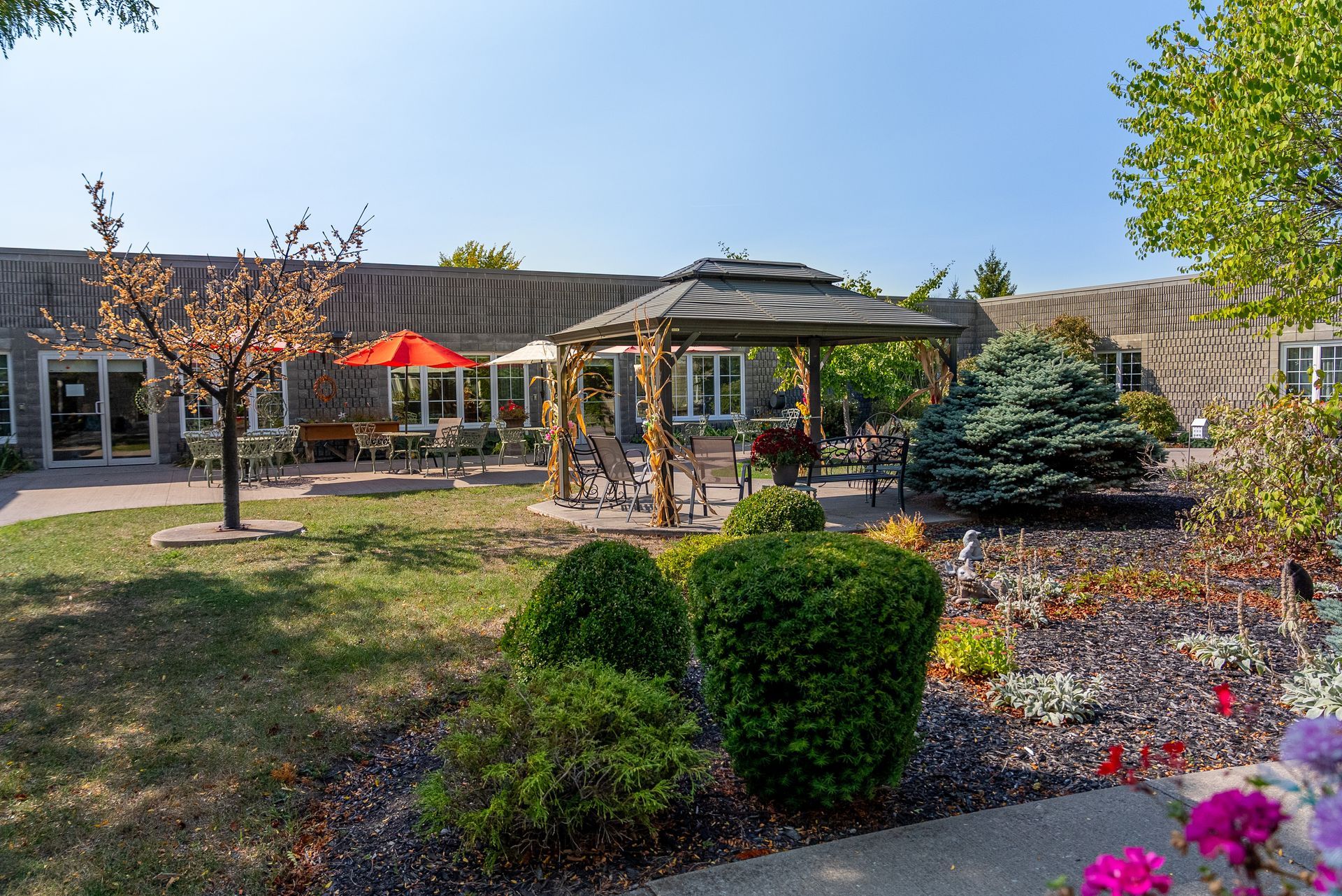 Courtyard garden with gazebo, red umbrellas, trees, and flower beds outside a building