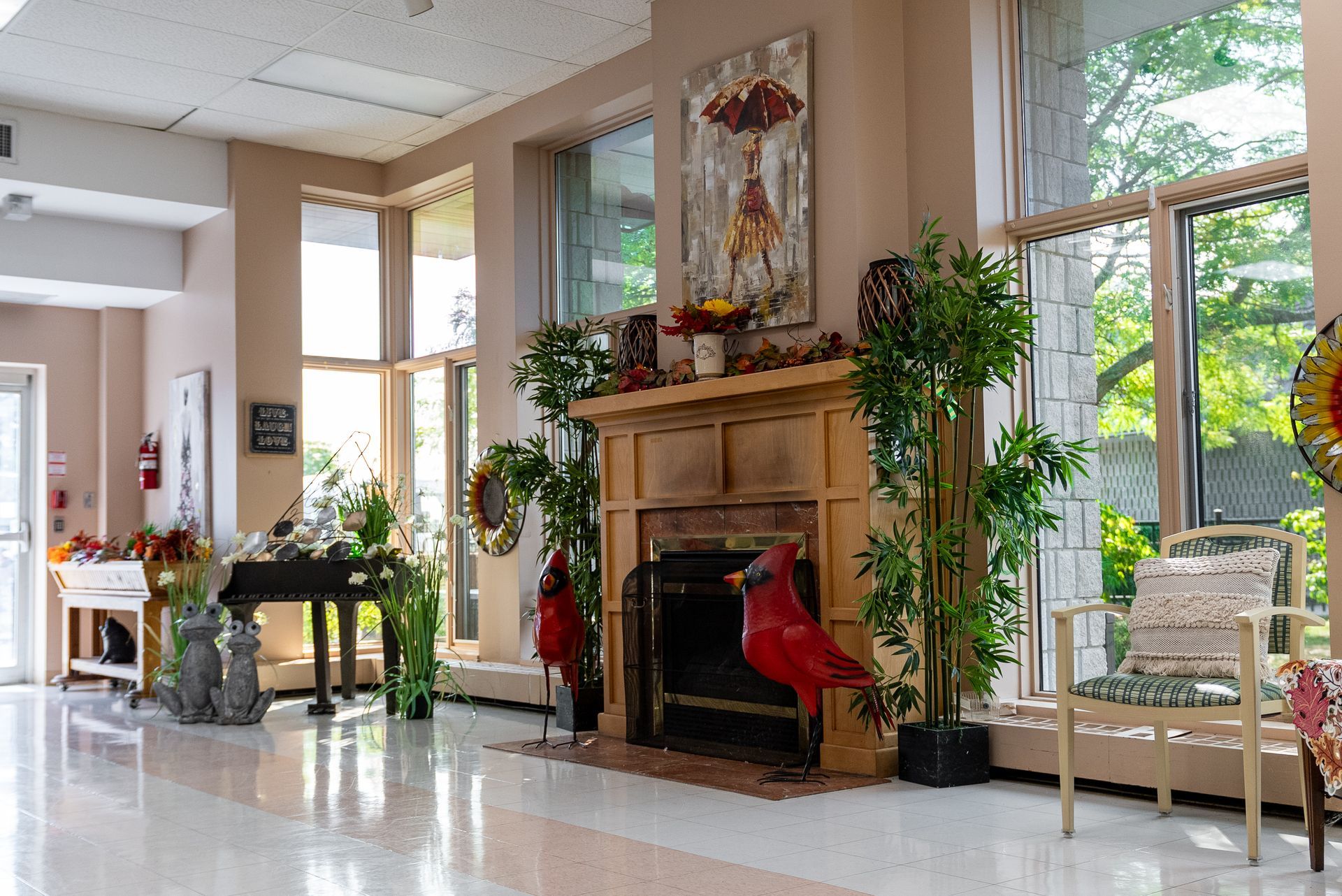 Bright lobby with a fireplace, tall windows, potted plants, and a piano near the entrance.