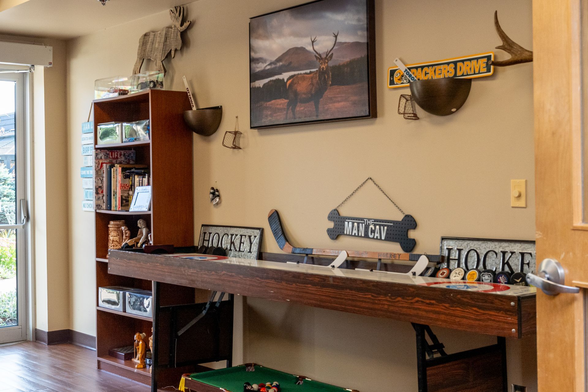 Home office with a long wooden desk, bookshelf, wall art, and a view of a patio door.