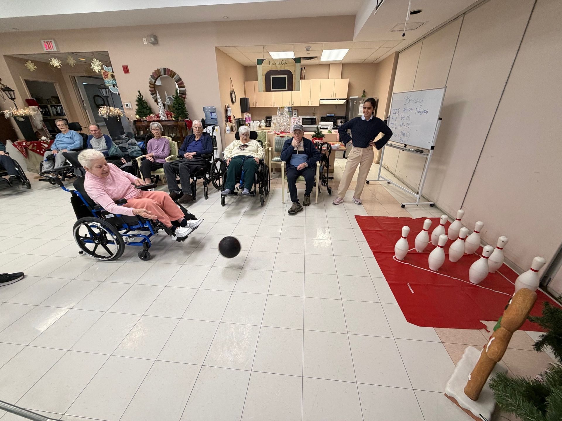 Indoor bowling game with seated spectators, a rolled ball, and pins set on a red mat