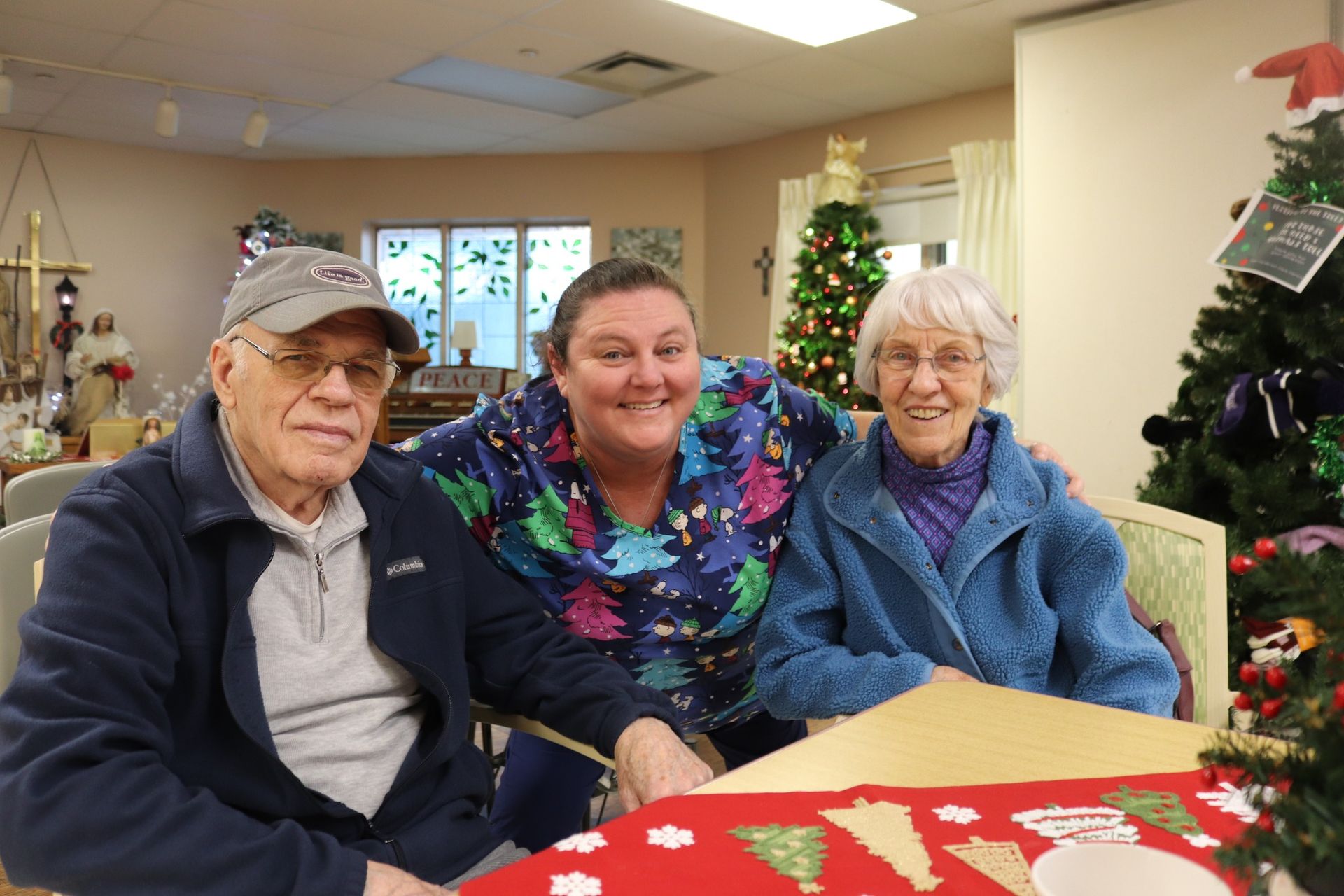 Three people smiling at a holiday table in a decorated indoor room with a Christmas tree nearby