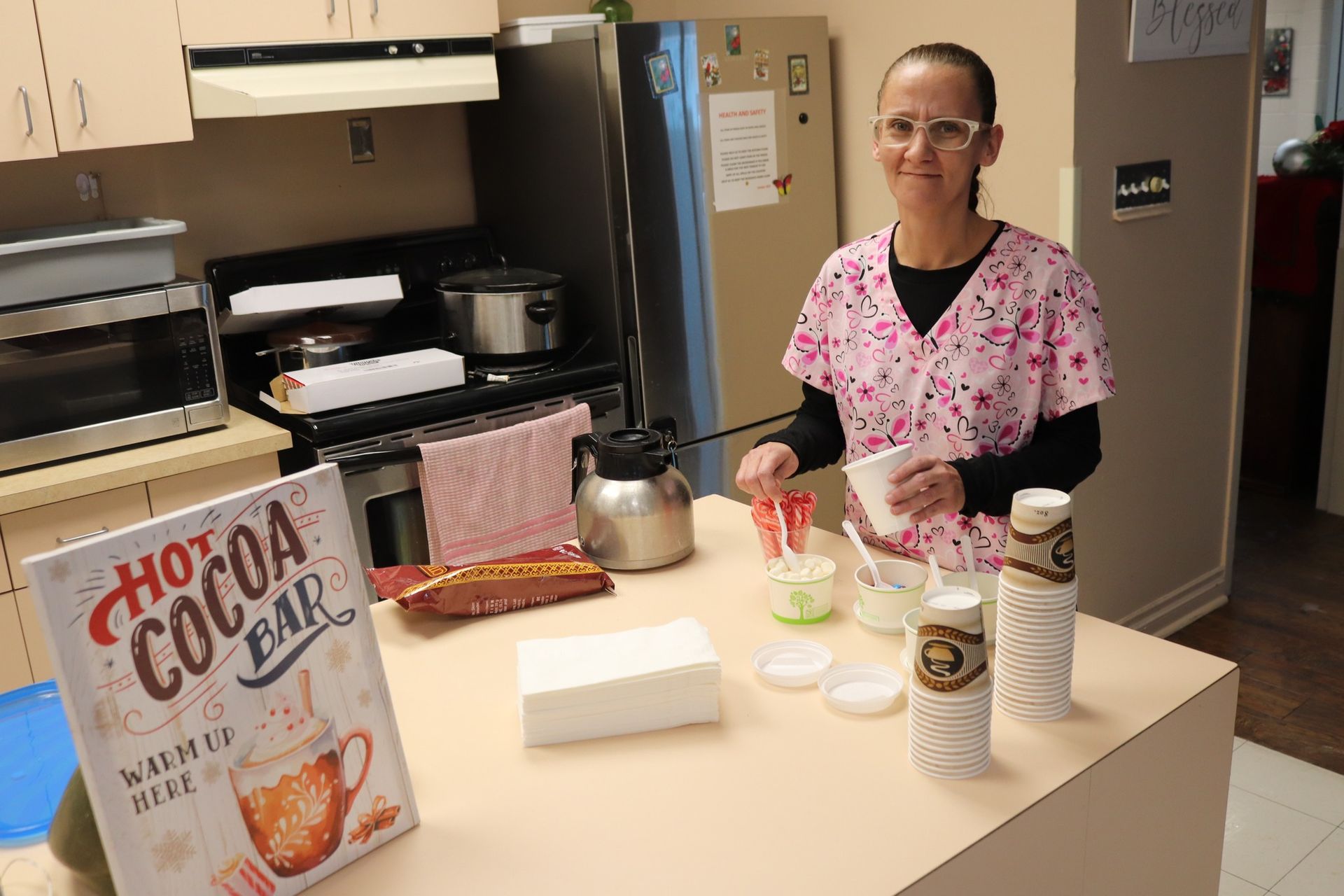 Woman in a kitchen standing behind a counter with baking ingredients, mixer, and cereal box.