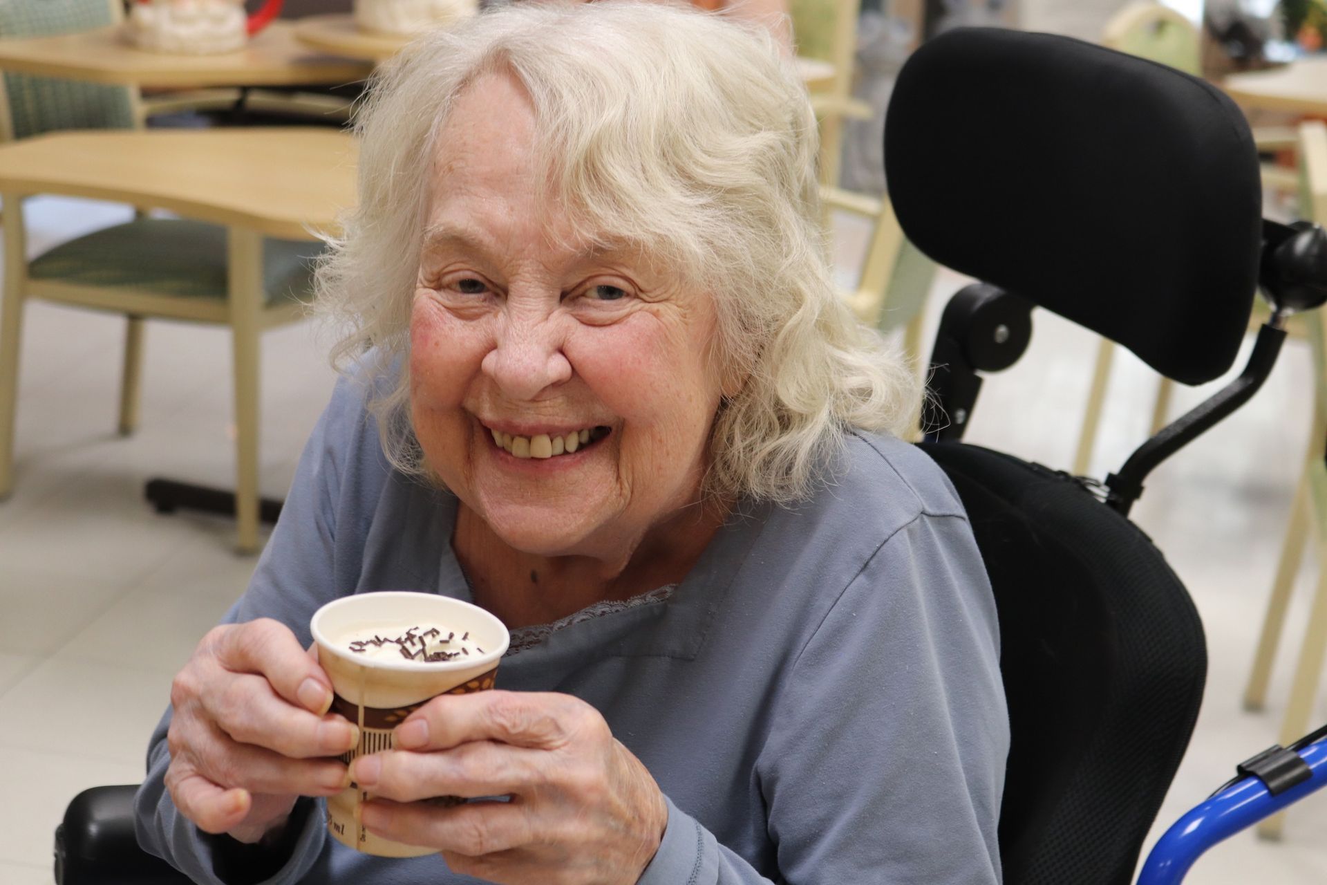Smiling woman in a wheelchair holding a small dessert cup in a bright room