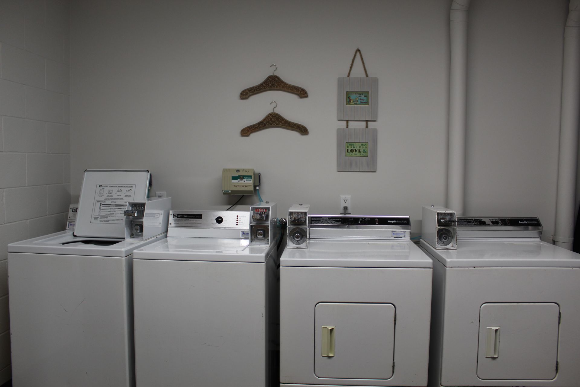 Laundry room with three white washers, two dryers, and wall-mounted signs on a gray wall