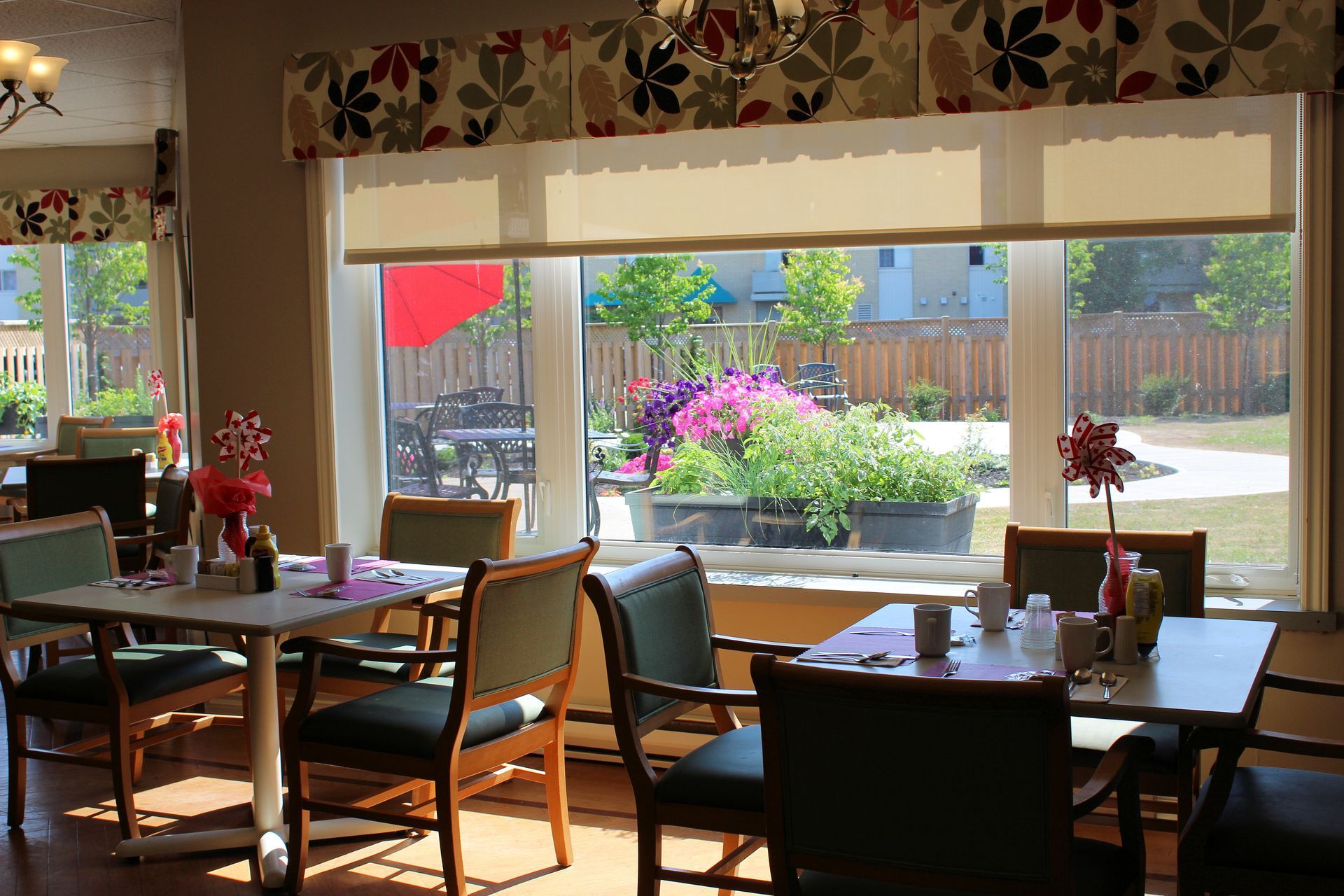 Sunlit café dining room with tables by large windows overlooking a flower-filled patio