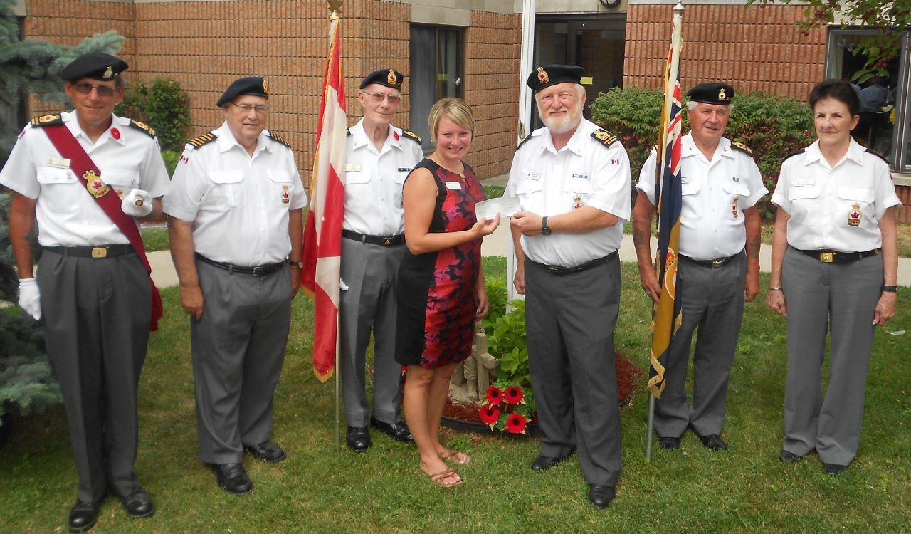 Group of uniformed people standing outdoors beside a memorial with flowers and a flag.