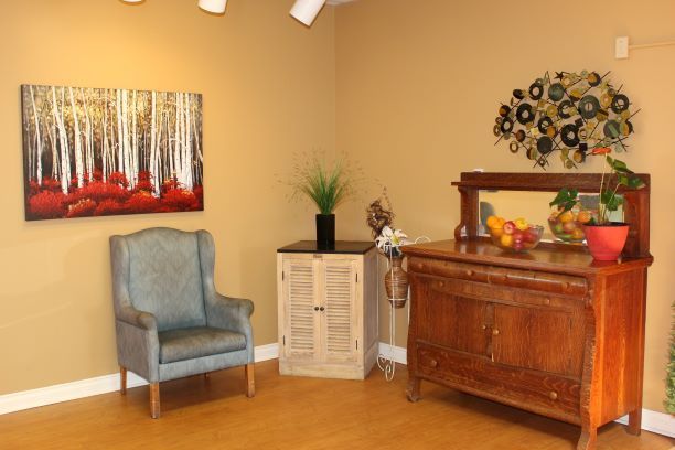 Cozy living room corner with blue chair, wooden cabinet, wall art, and decorative plants
