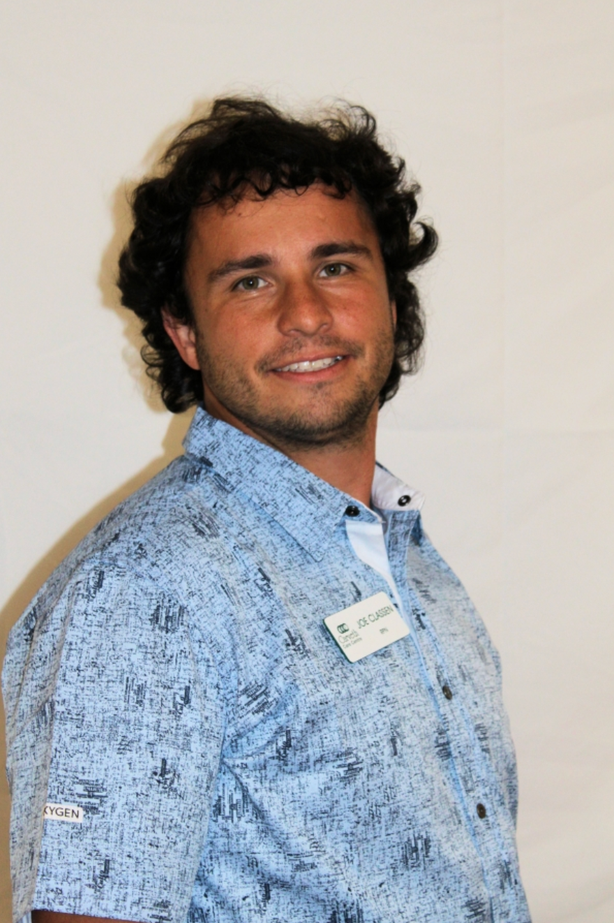 Smiling person in a light blue patterned shirt against a plain wall