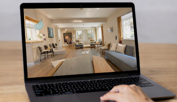 Laptop displaying a bright modern living room interior, with a hand on the keyboard.