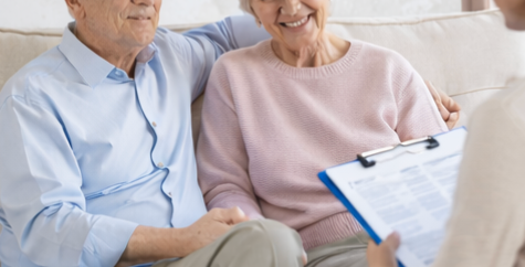 Older couple sitting on a couch while a doctor discusses paperwork with them