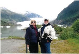 Two hikers standing by a glacier lake with mountains in the background