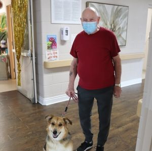 Masked man standing indoors with a small dog on a leash in a hallway