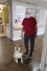 Masked person in red shirt walking a dog in a hallway