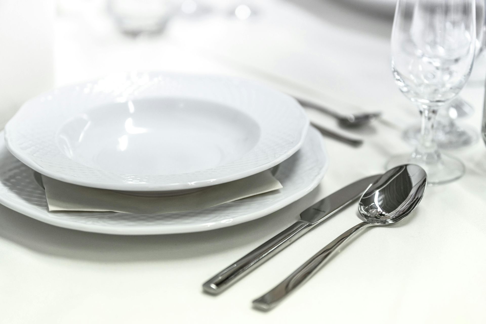 Elegant white table setting with plates, silverware, and a glass on a white tablecloth