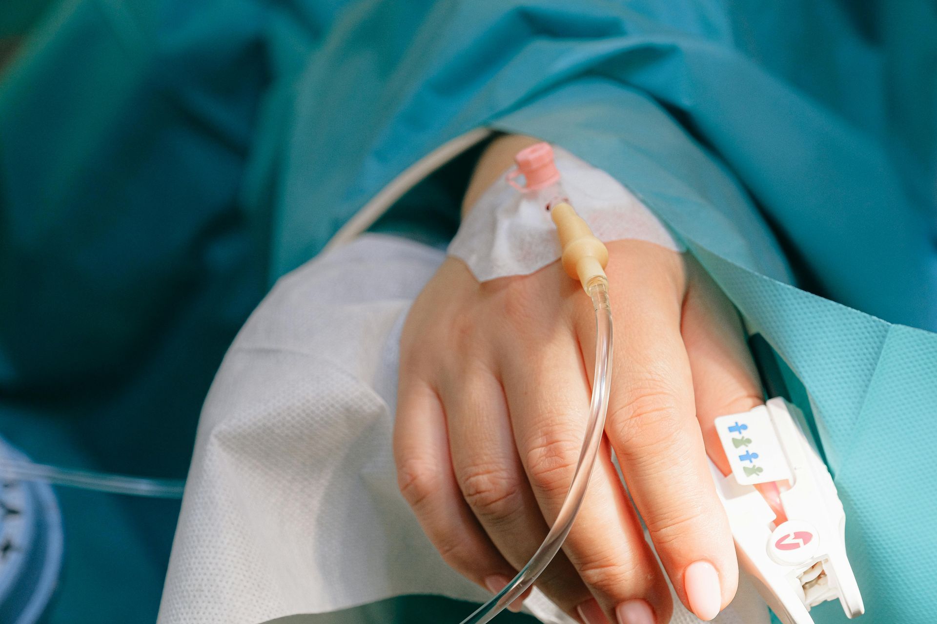 Hand with IV cannula and tape in a hospital bed, covered by blue surgical drape