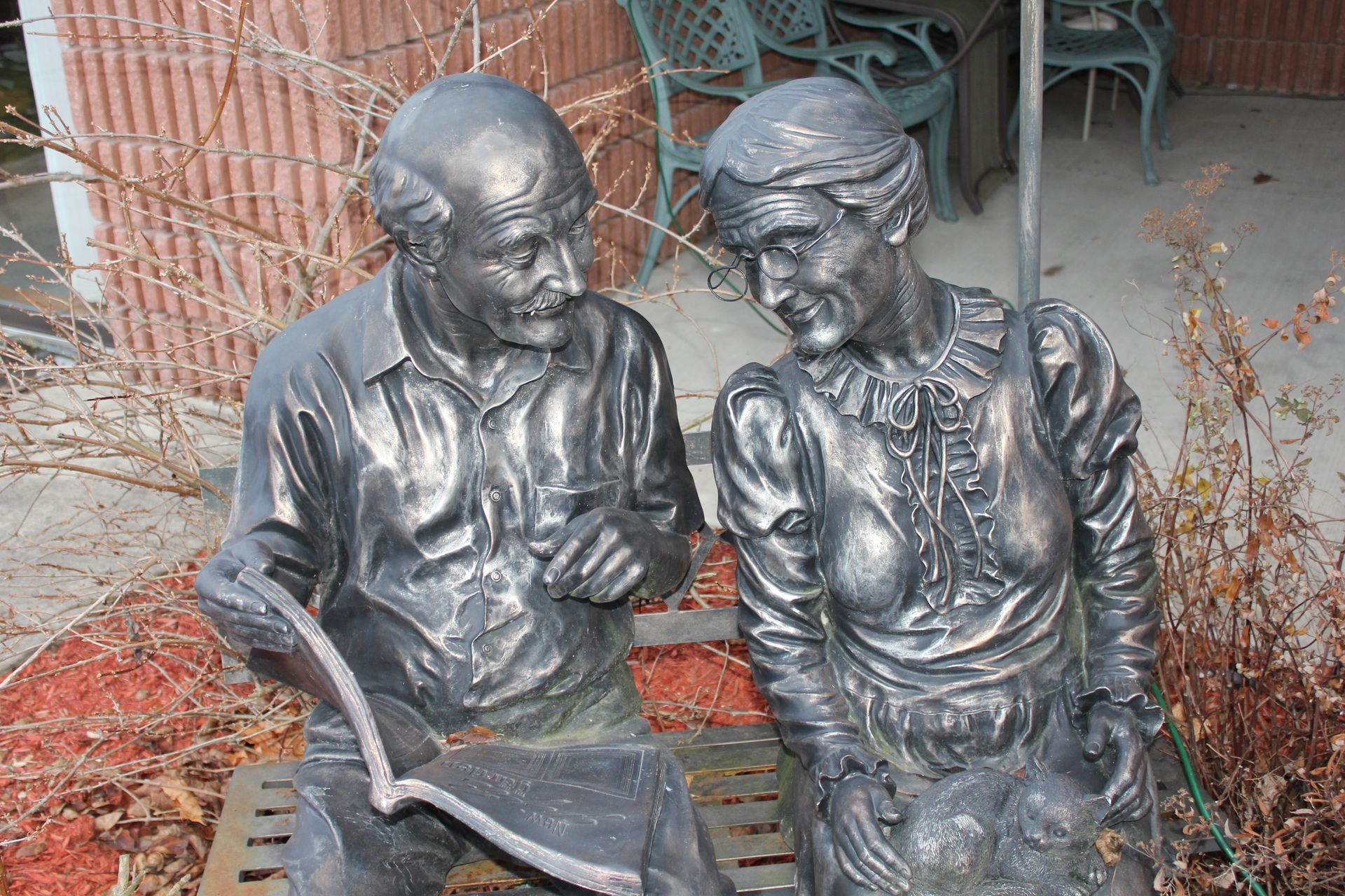 Two seated bronze statues reading together on a bench amid autumn leaves