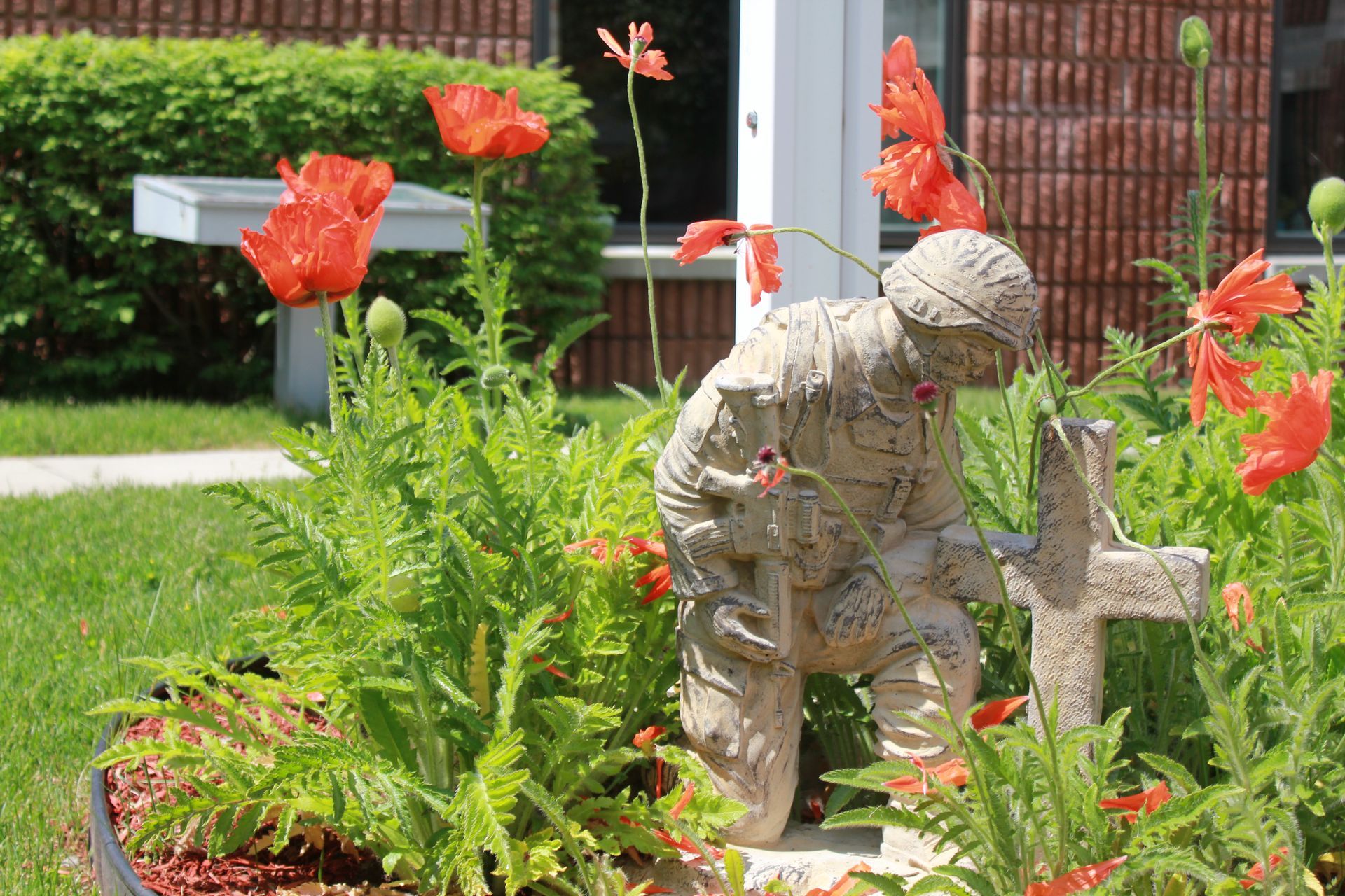 Garden statue among red flowers and green foliage beside a brick path