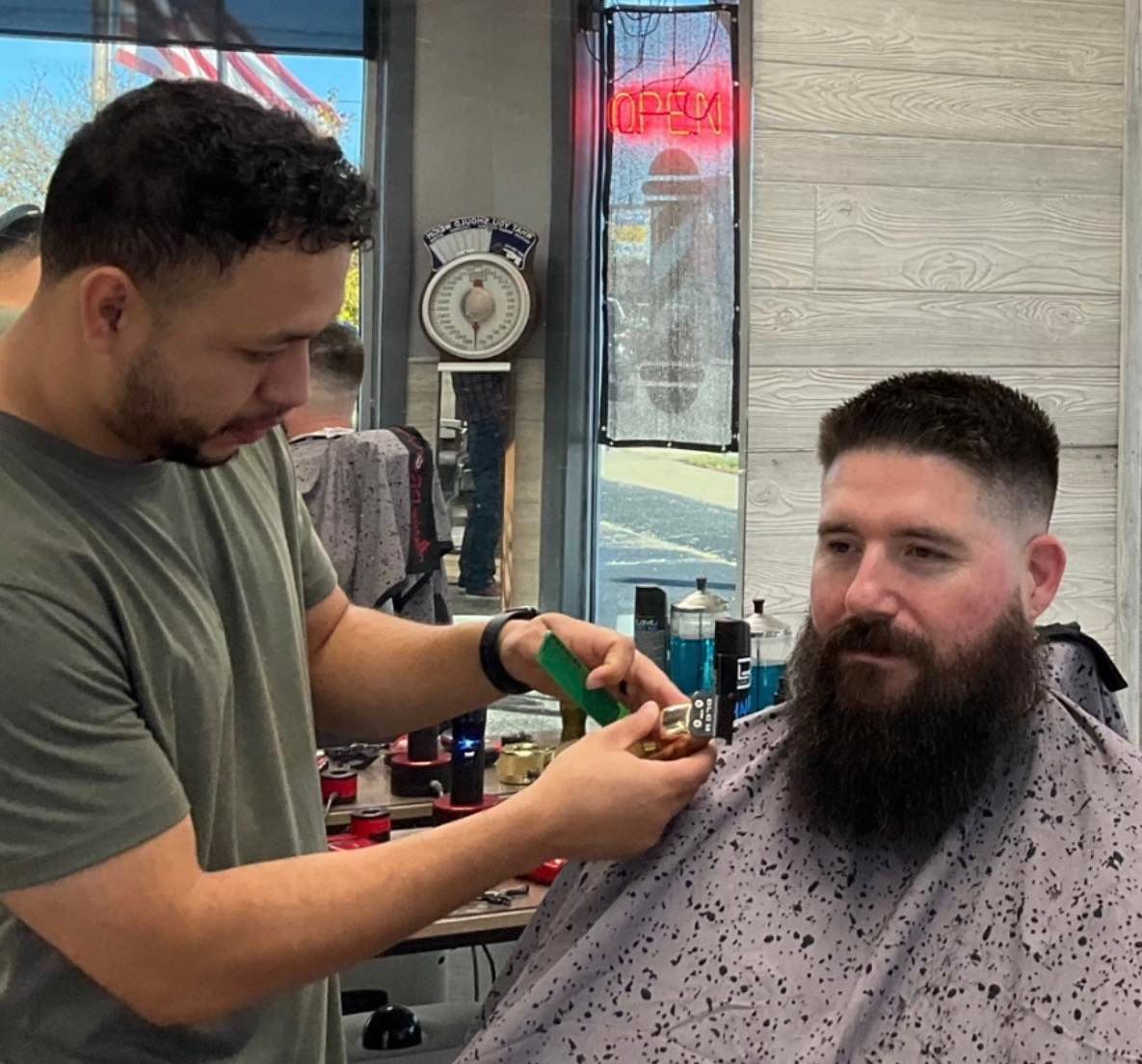 A man with a beard is getting his hair cut at a barber shop.