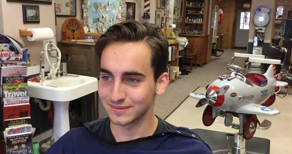 A young man is getting his hair cut in a barber shop.