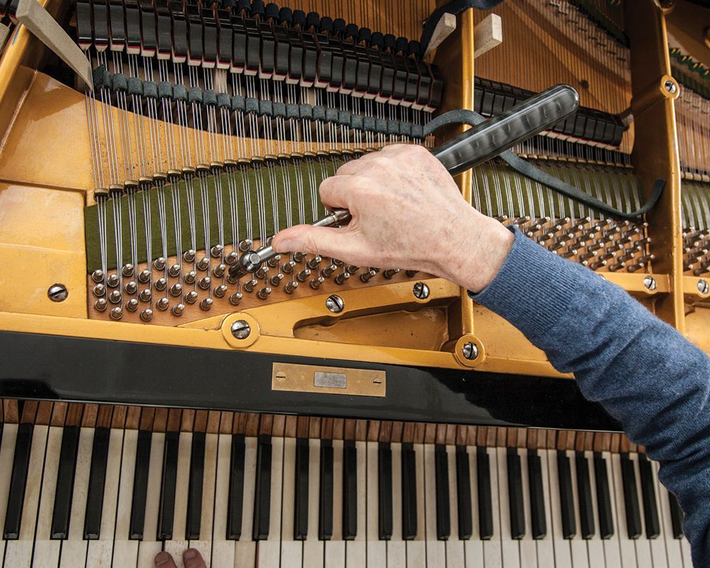 Closeup of piano tuner working on a grand piano with specialized tools.