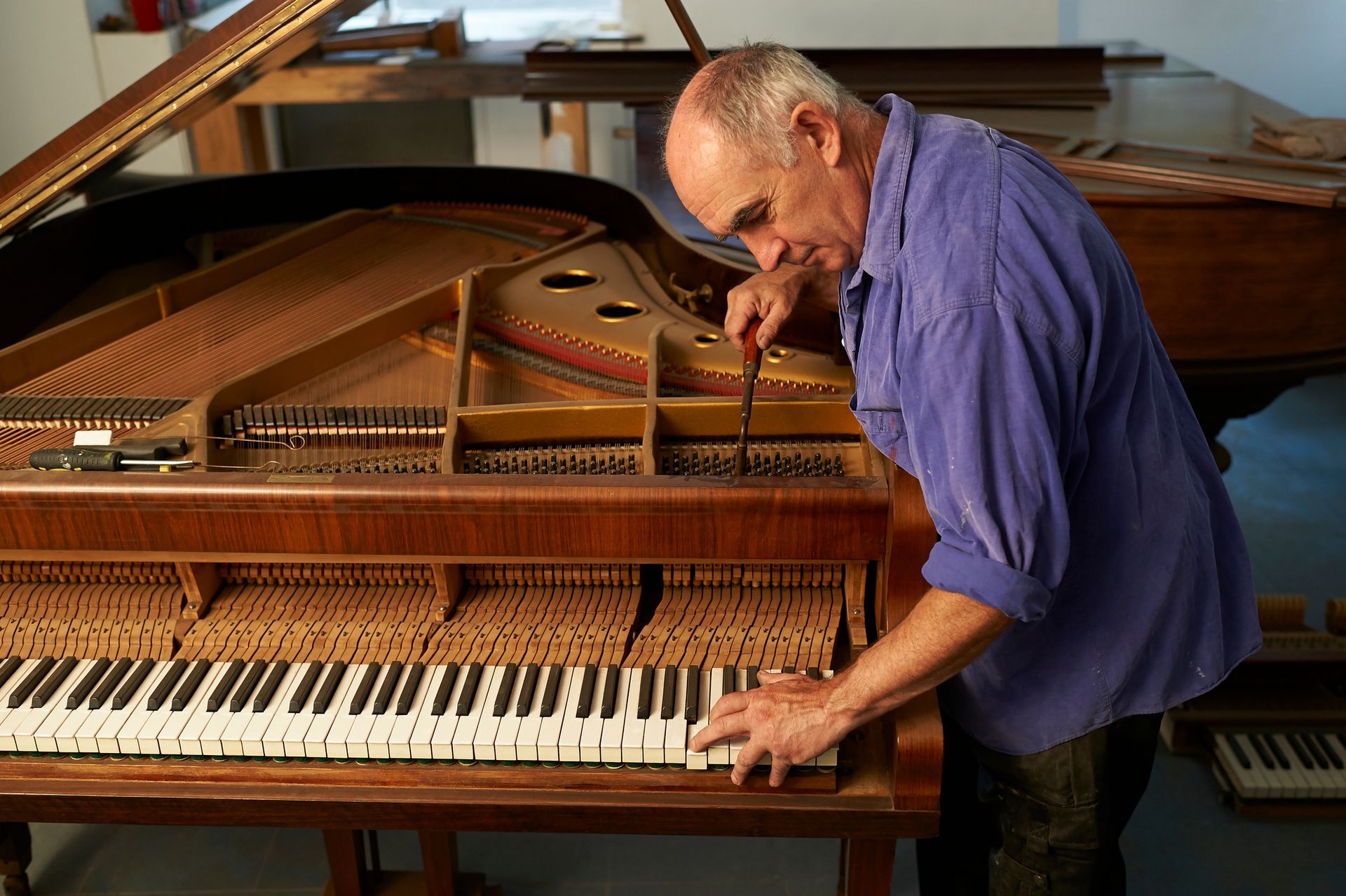 A man is tuning a piano in his workshop. A man is tuning a piano in his workshop.