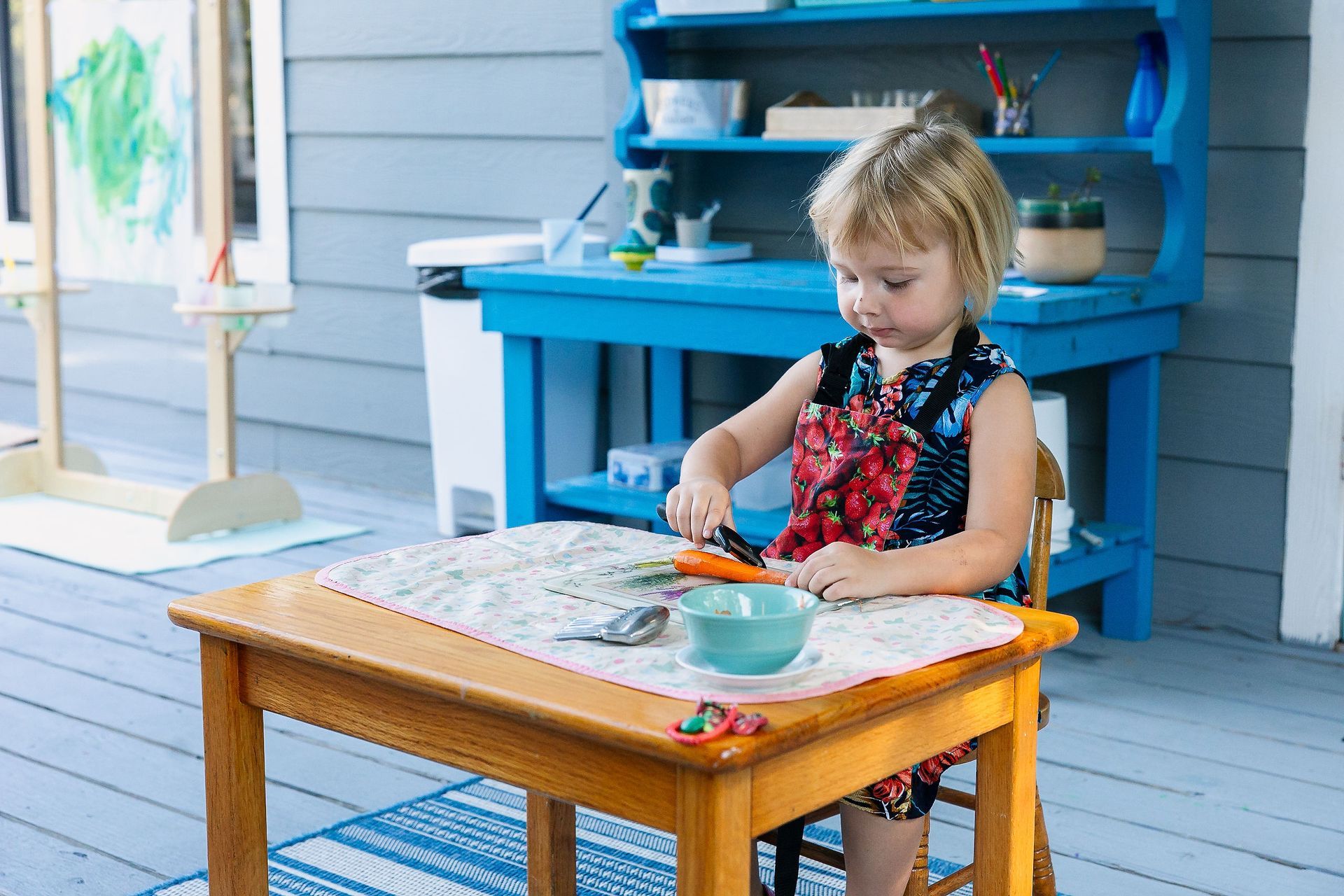 Child working at a blue outdoor table on a porch