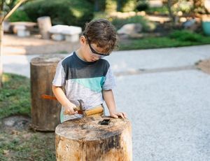 Montessori child hammering wood with focus, showing persistence and independence in work.