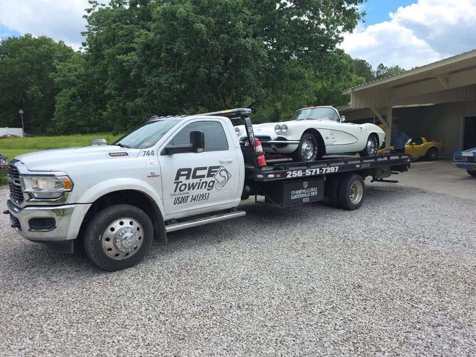 White tow truck with a white vintage Corvette on its flatbed, near a building.