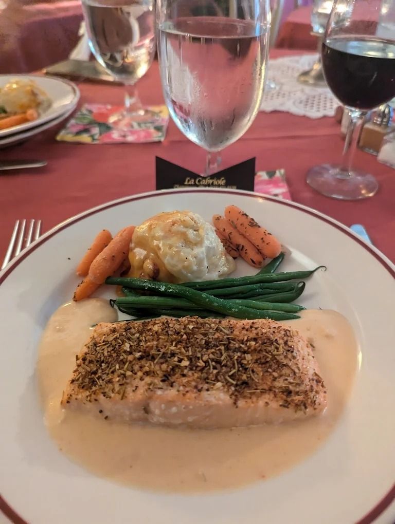 Salmon with vegetables and sauce on a plate, set at a table with glasses and wine.
