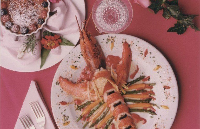 Macaroni and cheese in a red dish, topped with cheese and rosemary, on a rustic wooden table.
