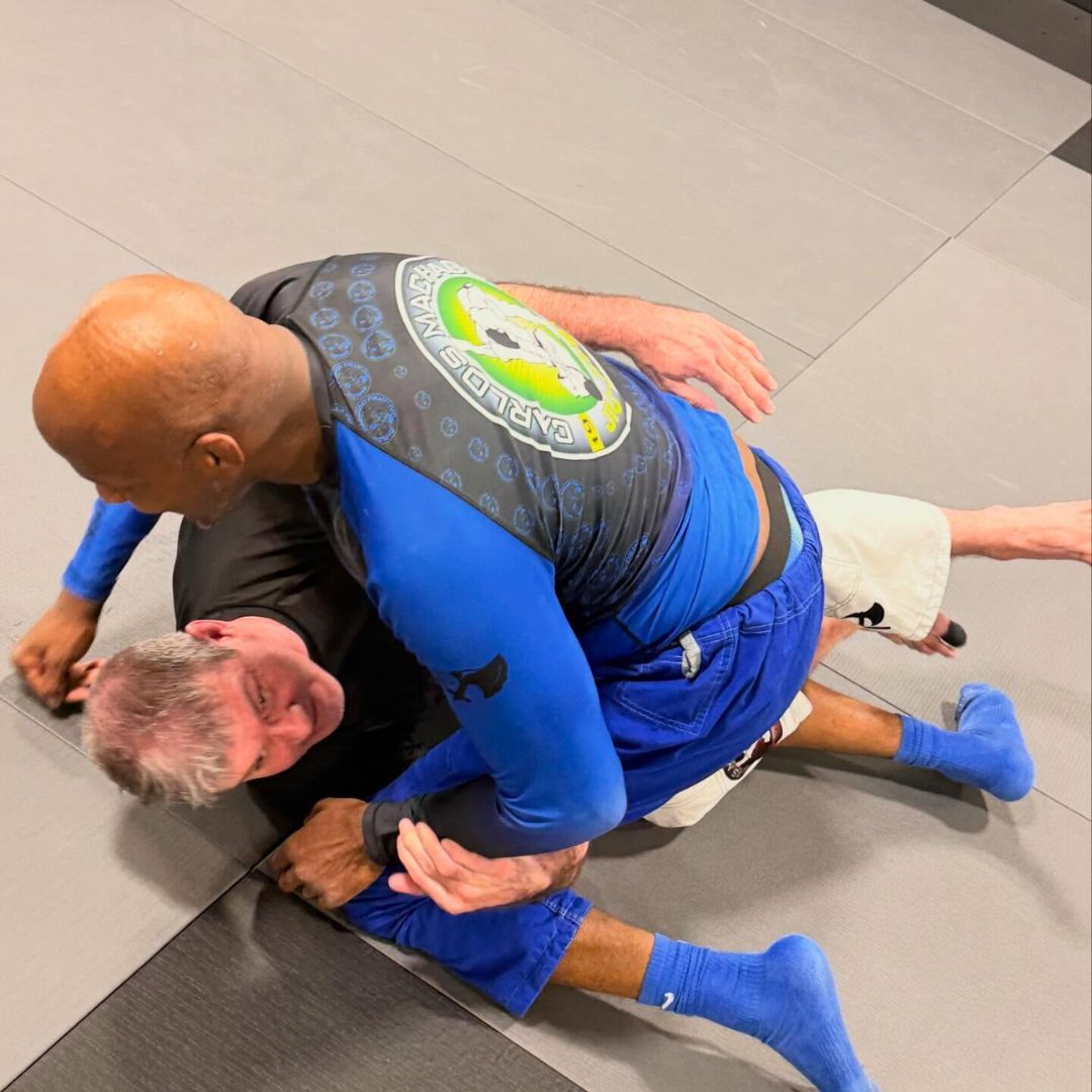 Two men grappling on a mat, one in blue, the other in black.