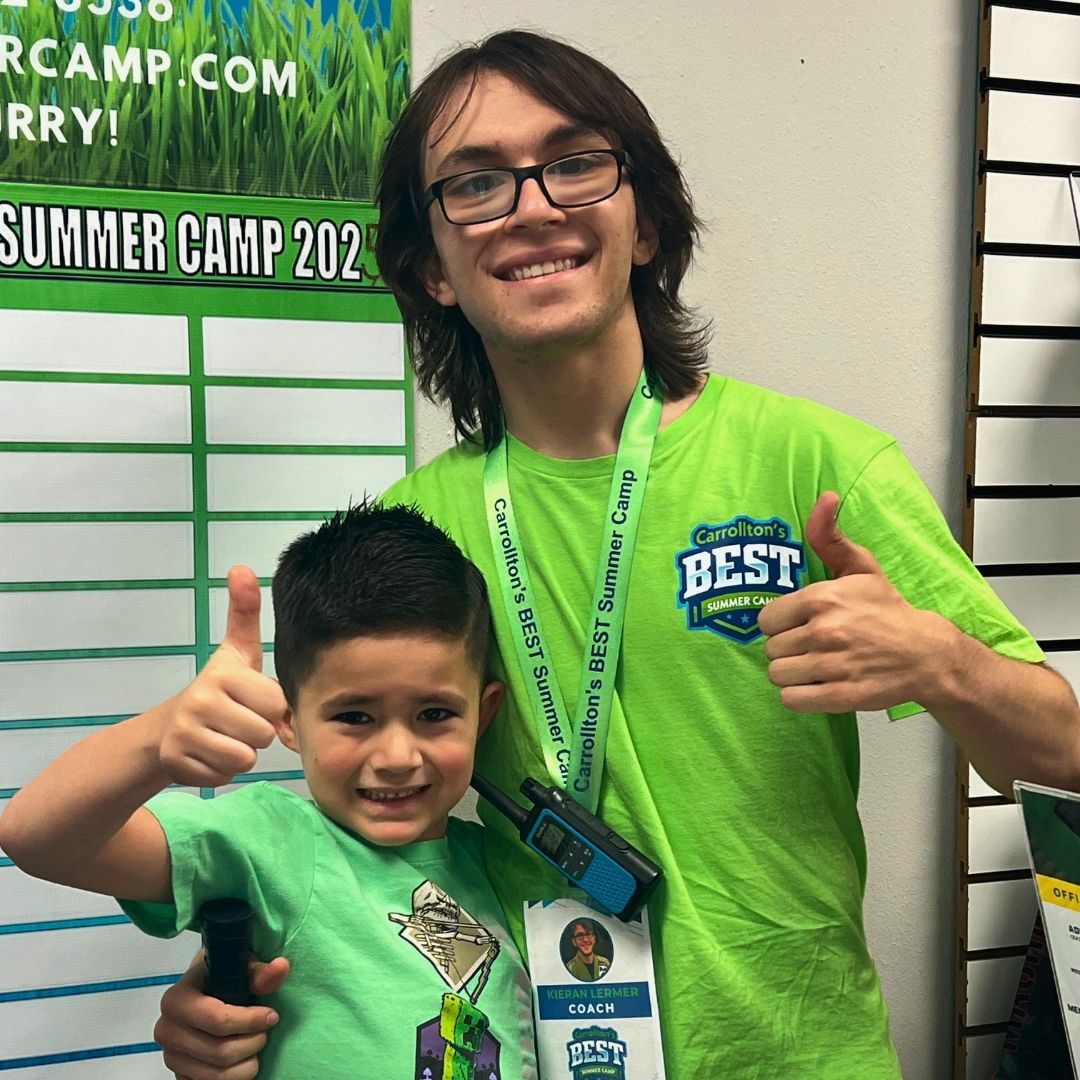 Two people giving thumbs up: a young boy and a taller person, both wearing green shirts.