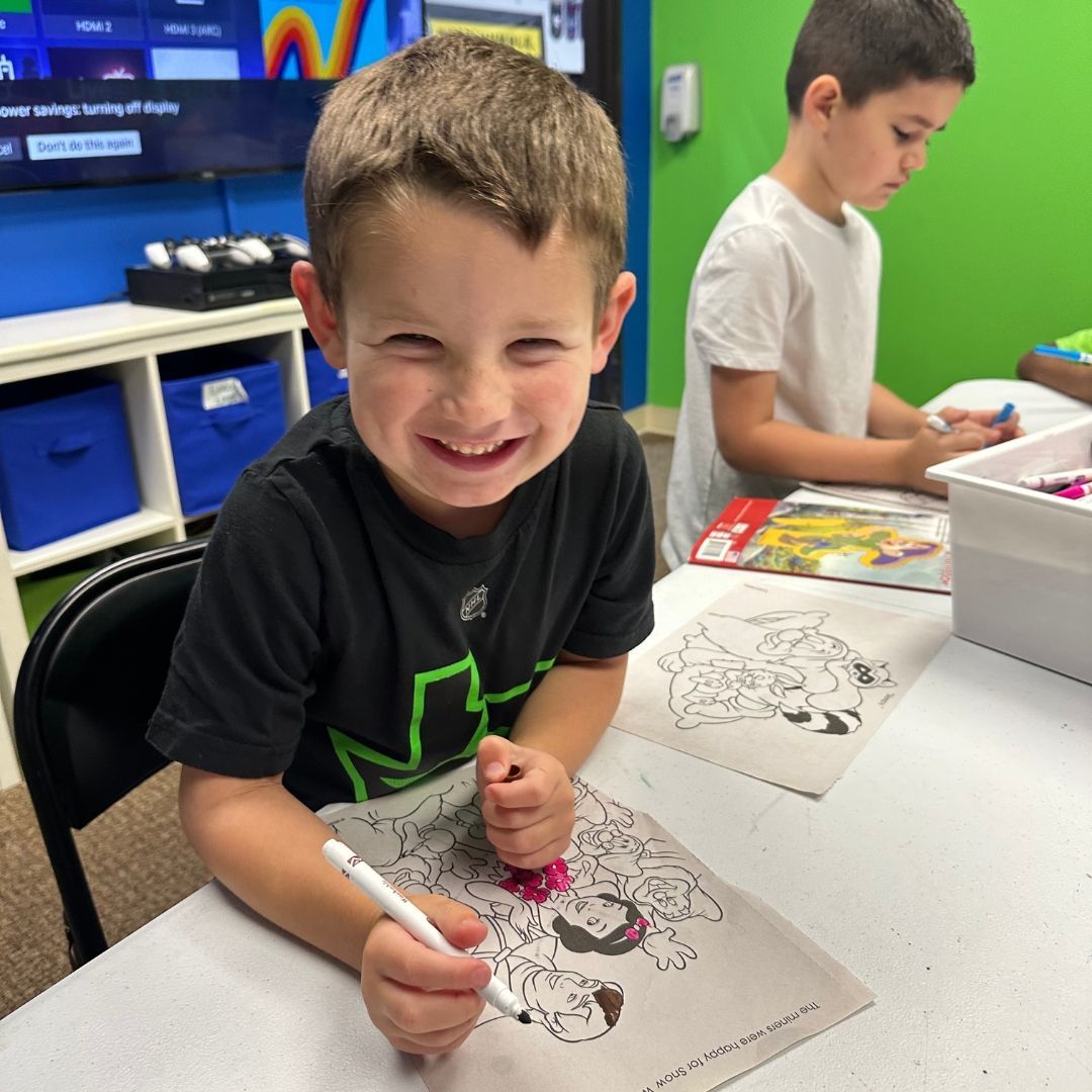 Boy smiling, coloring a Teenage Mutant Ninja Turtle picture, in a classroom setting.