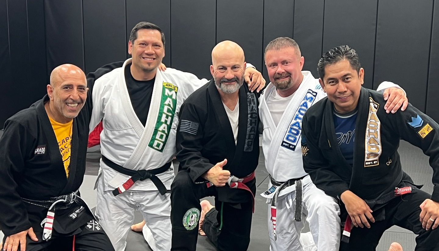 Five people in blue and green martial arts attire, smiling, with flags in background.