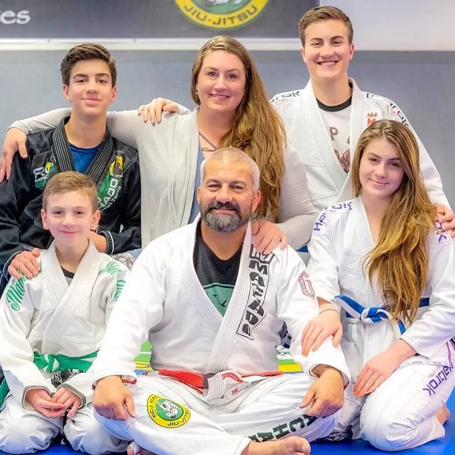 Family posing in a jiu-jitsu gym. Two adults and four children, some in gis, smiling.