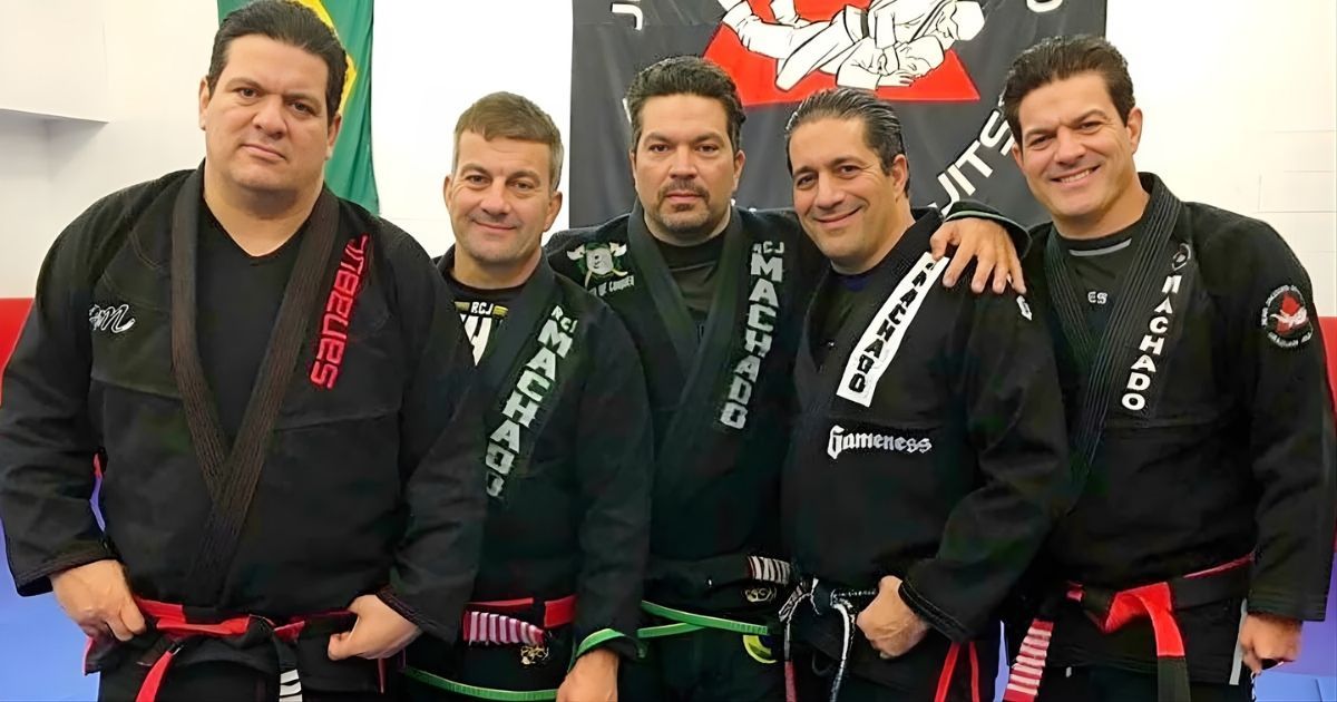 Five men in black gi uniforms, red and green belts, posing with arms around each other.