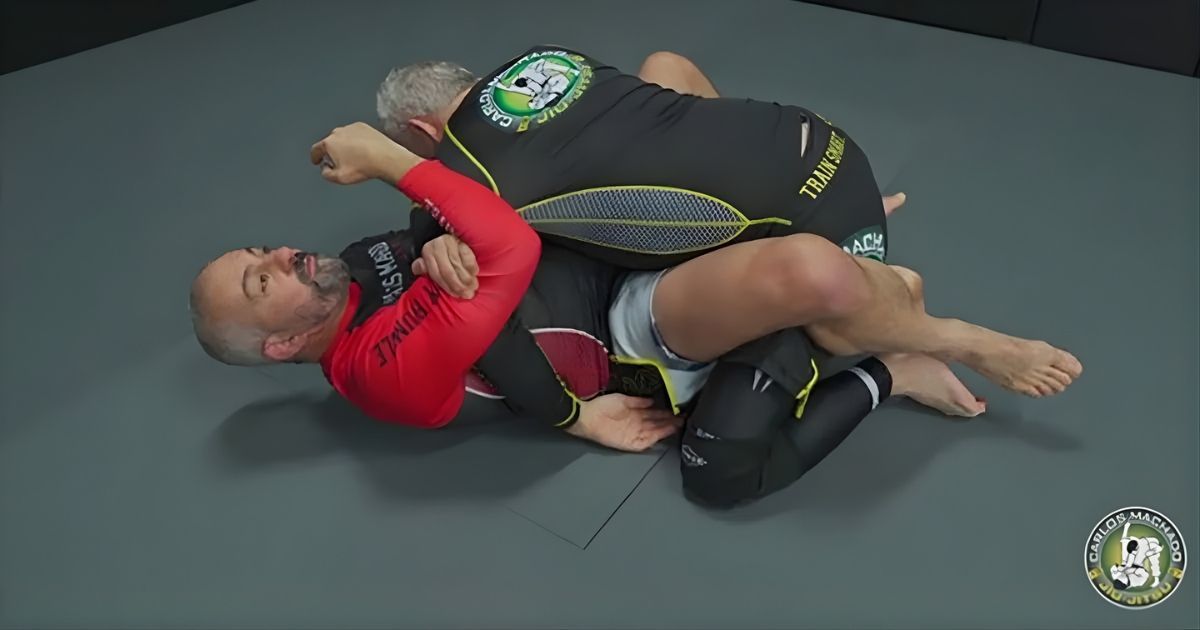 Two men grappling on a mat; one in red and black, the other in black and green, executing a leg lock.